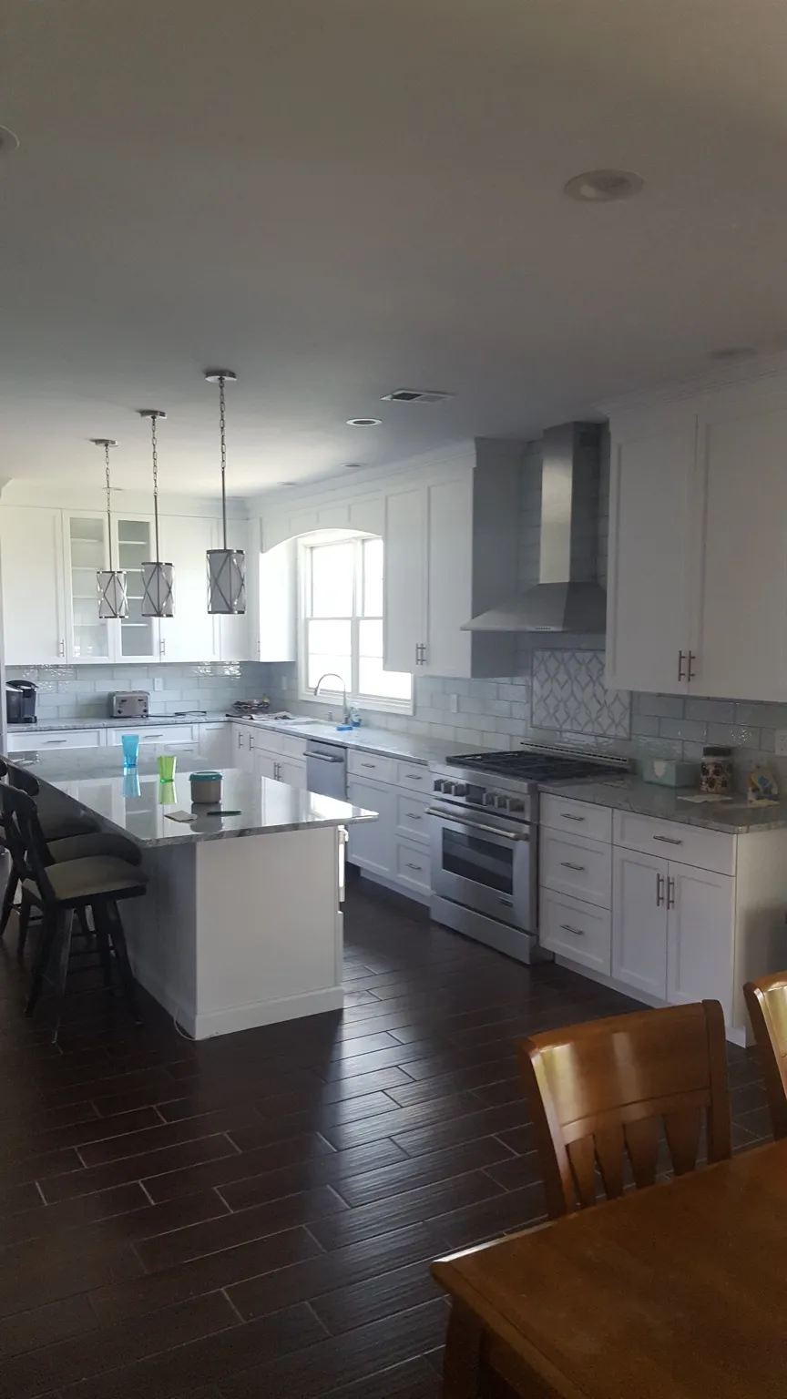 Bright white custom kitchen with island, tile backsplash, pendant lights, and dark flooring