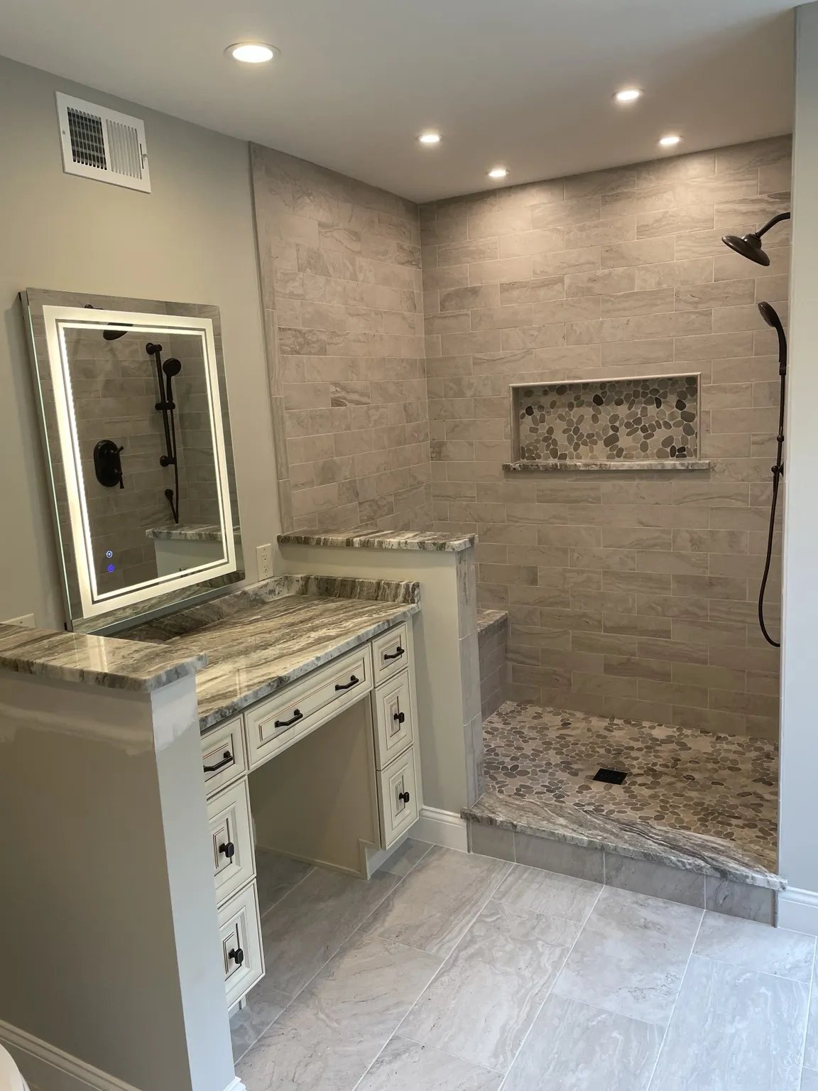 Luxury bathroom with custom open shower, pebble floor, vanity, and illuminated mirror
