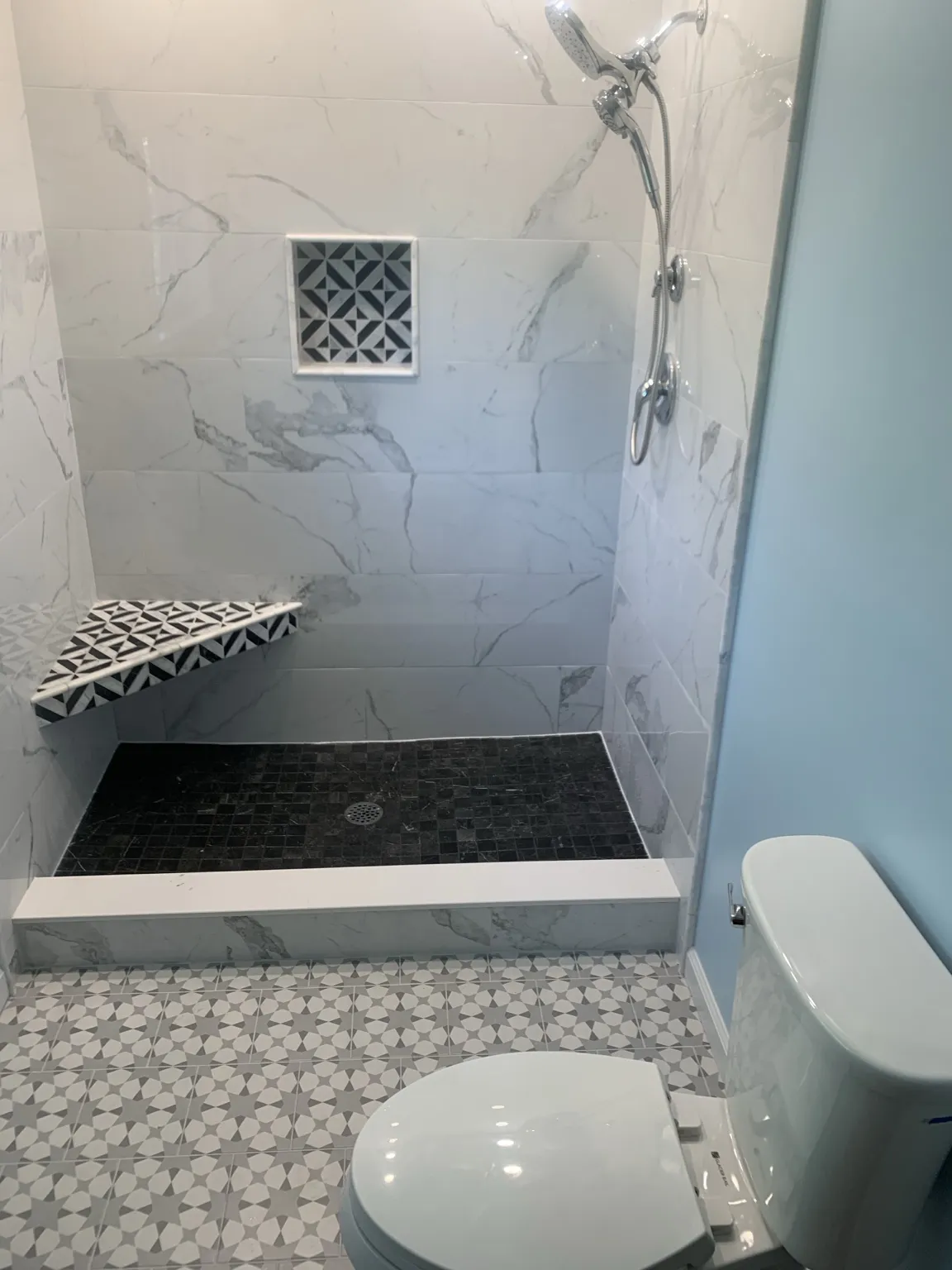 Modern marble-look tiled shower with geometric niche, bench, and patterned bathroom floor