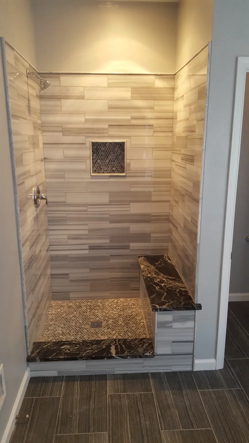 Walk-in shower with striped tile, pebble floor, niche, and granite bench