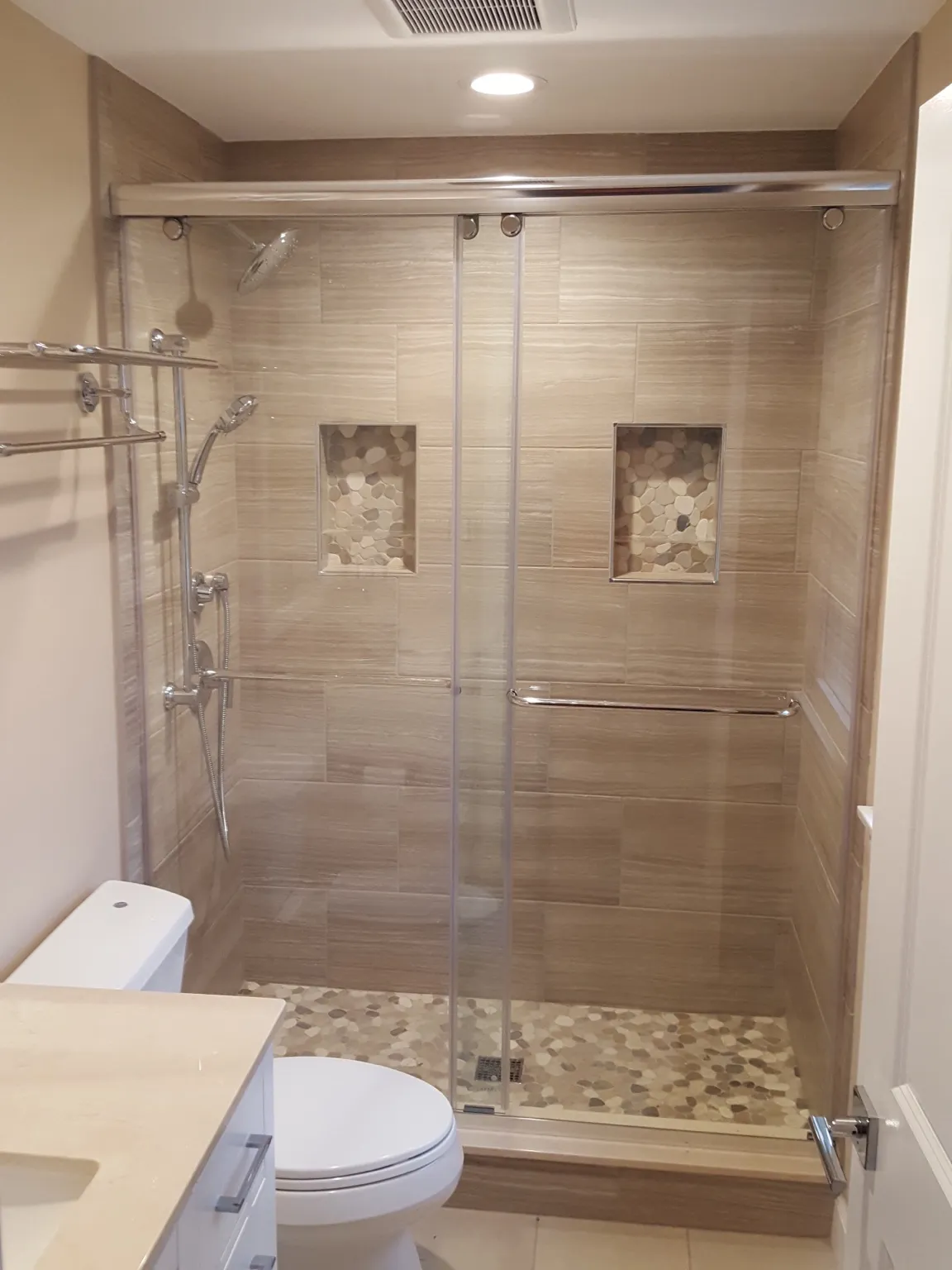 Glass enclosed shower with double niches and pebble tile floor