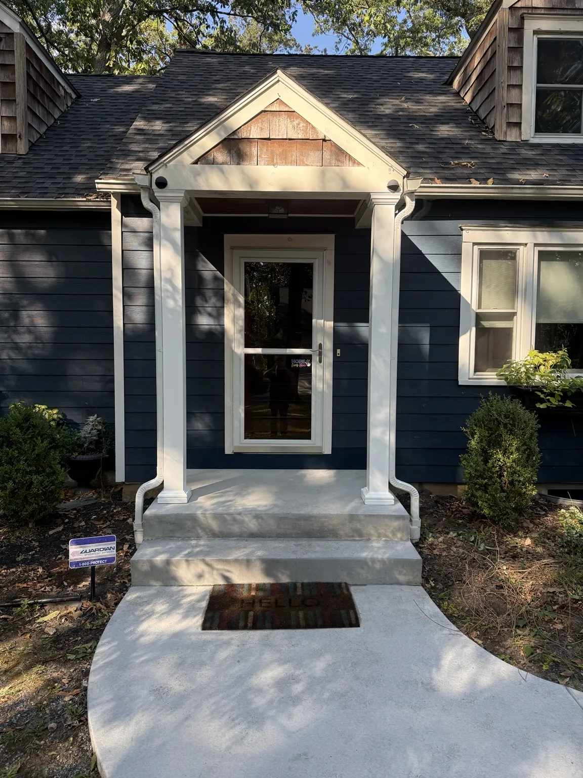 Completed white front portico with columns, gutters, lighting, and concrete walkway